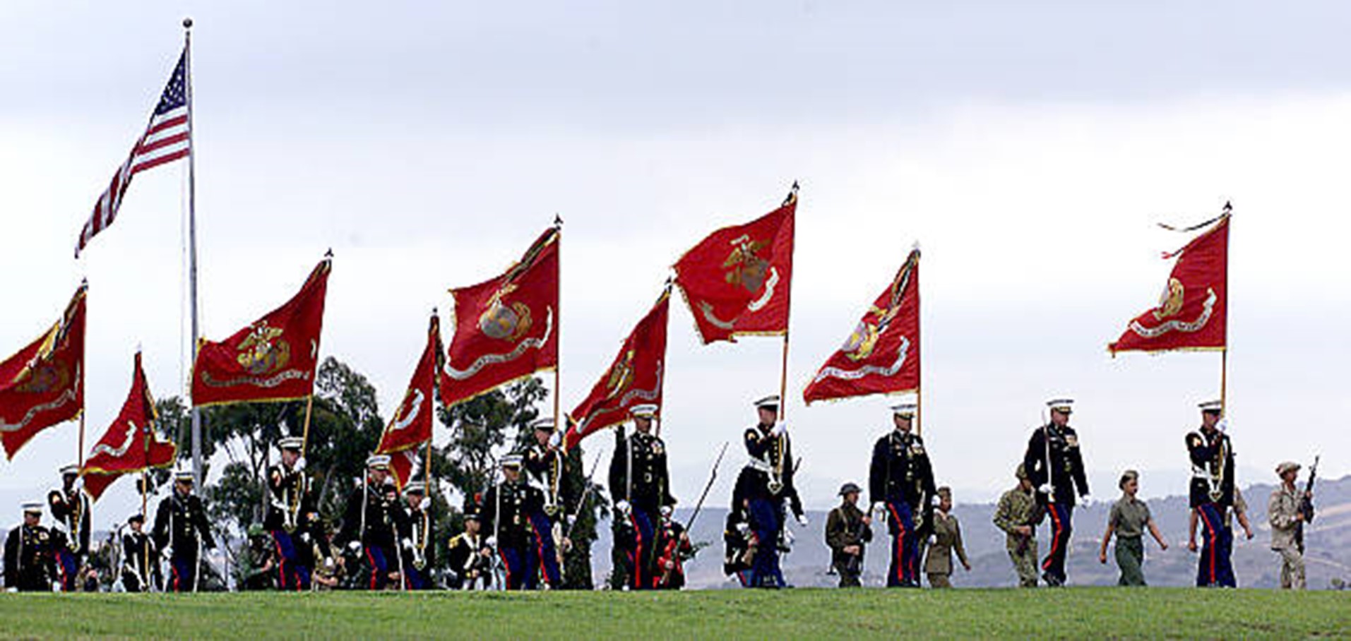 USMC in dress blues carrying Marine Corps flags in a ceremony of some kind of soldiers through the years.